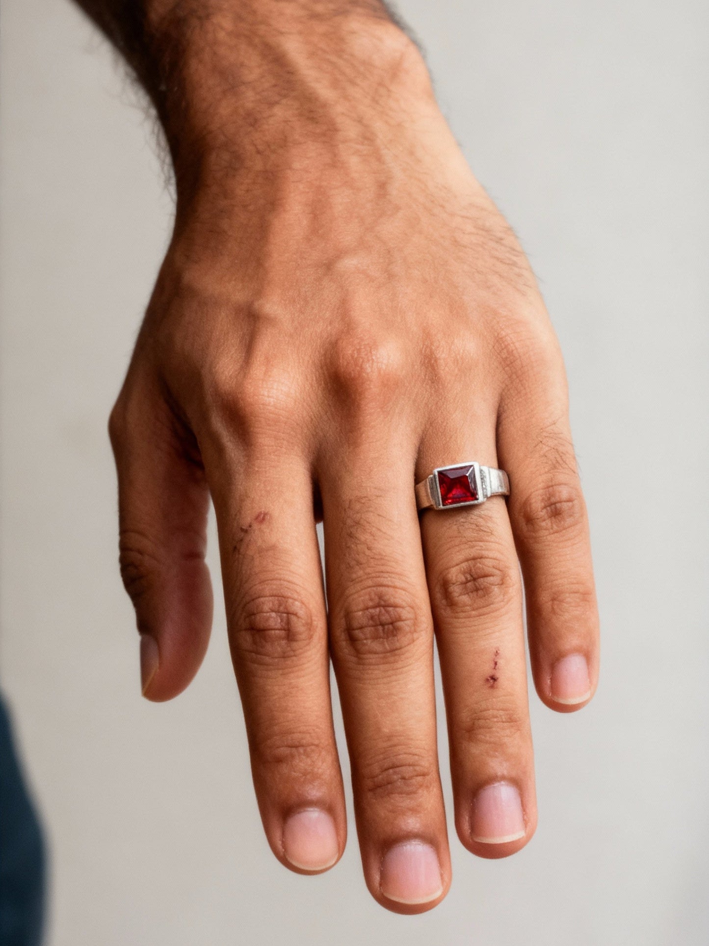 Hand wearing a ring with a red gemstone on a plain background