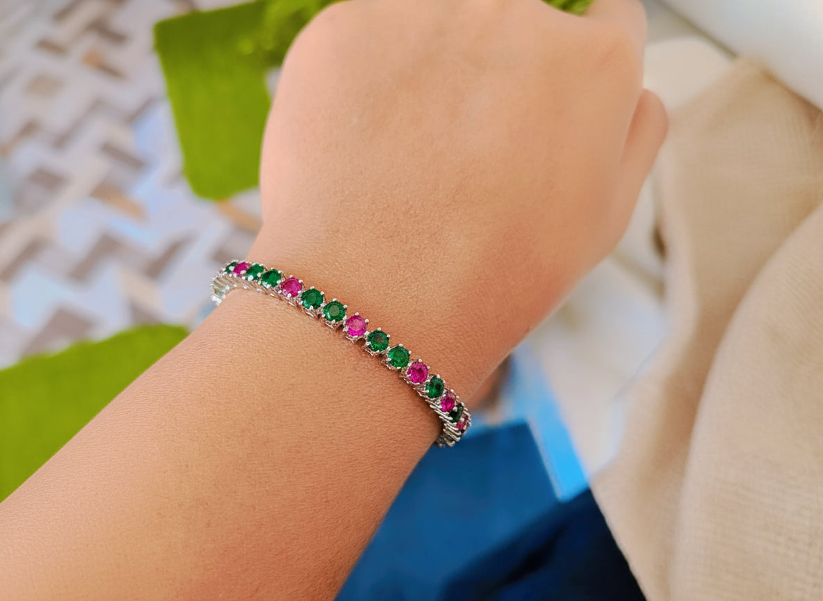 Bracelet with green and pink gemstones on a wrist against a blurred background
